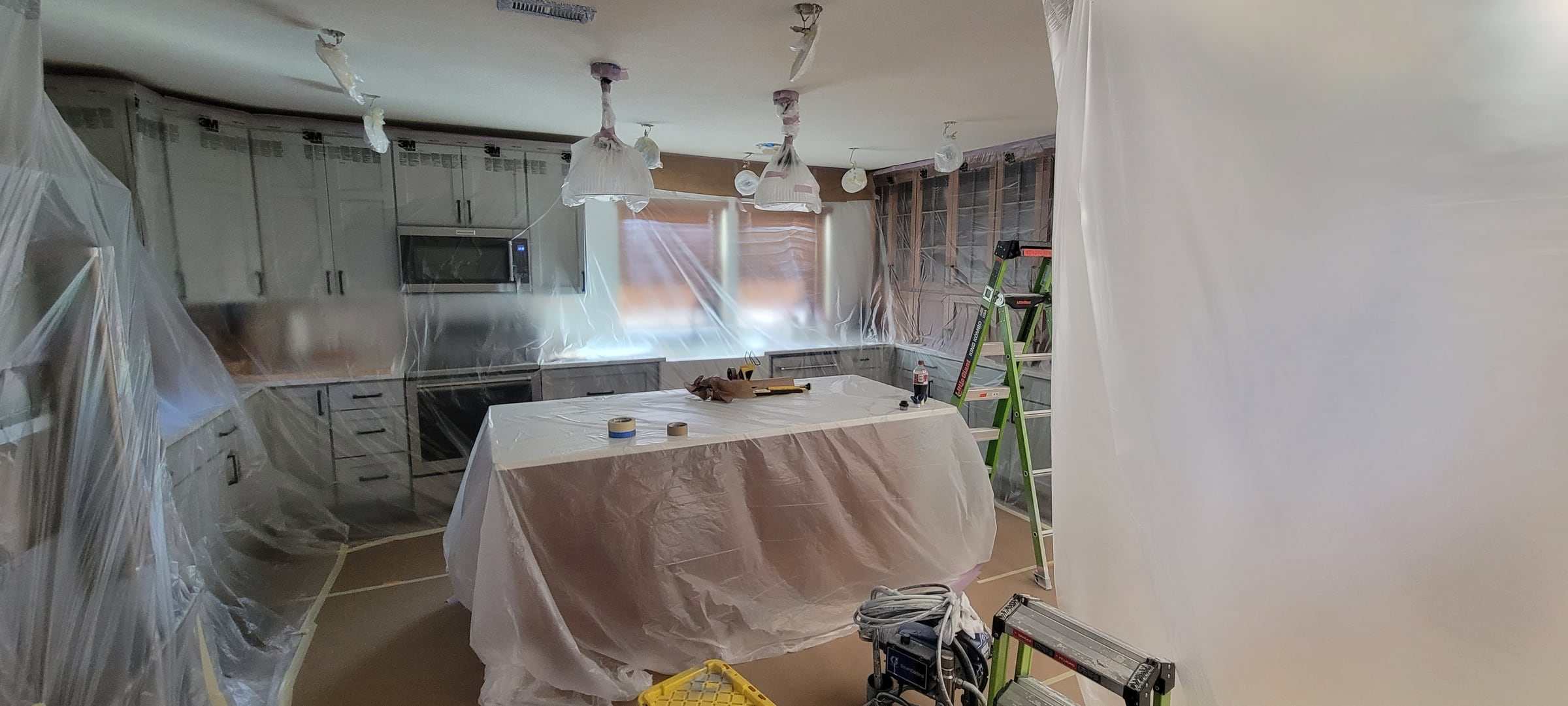 Kitchen with counters, island, appliances, windows and floor covered in plastic and paper, cabinets left exposed for finishing