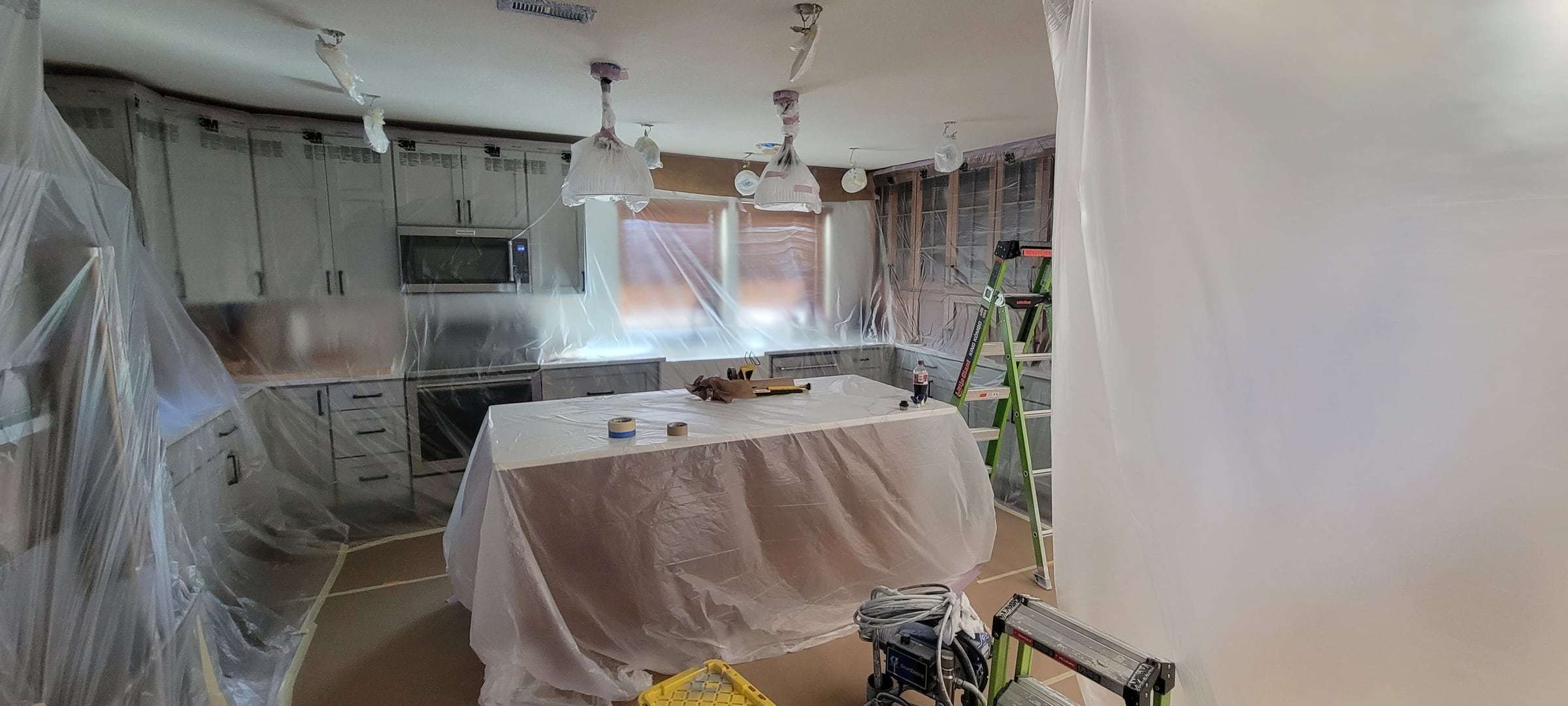 Kitchen with counters, island, appliances and floor covered in plastic and paper before cabinet finishing