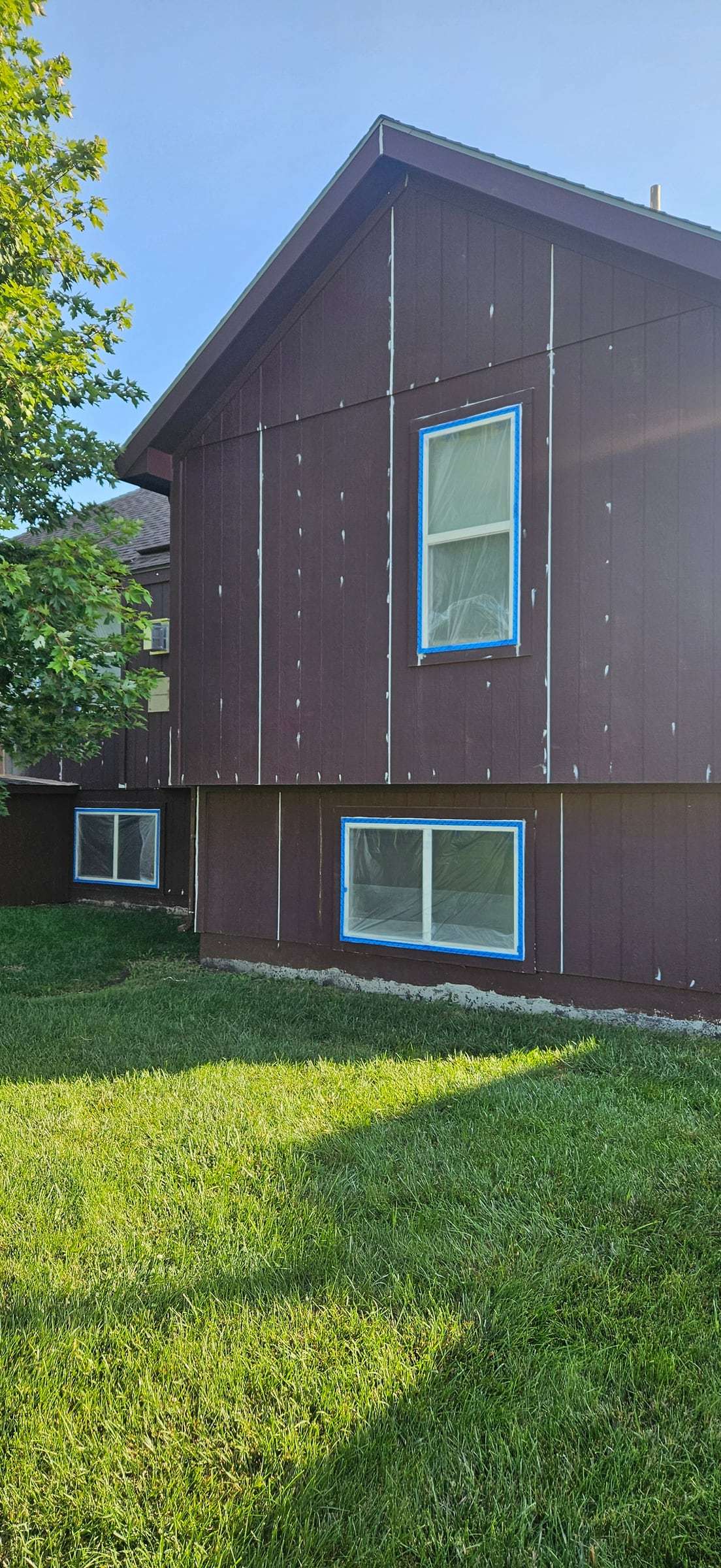 Back elevation with windows masked in blue tape and film and filled nail holes on the siding