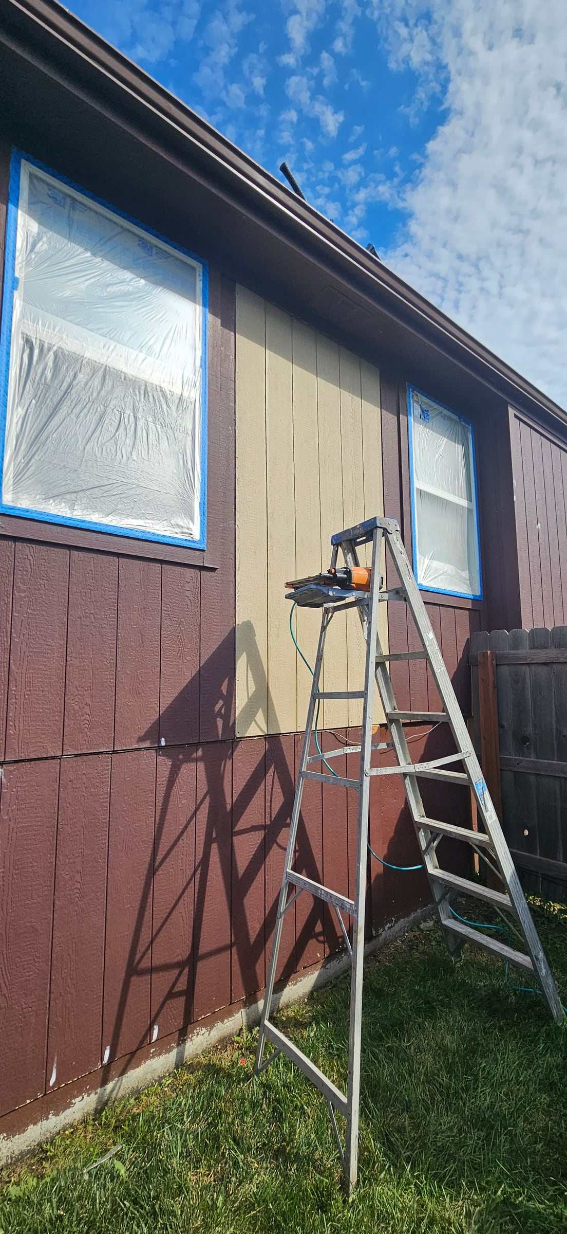 New unpainted siding panel installed between two windows on a home, with a ladder in front