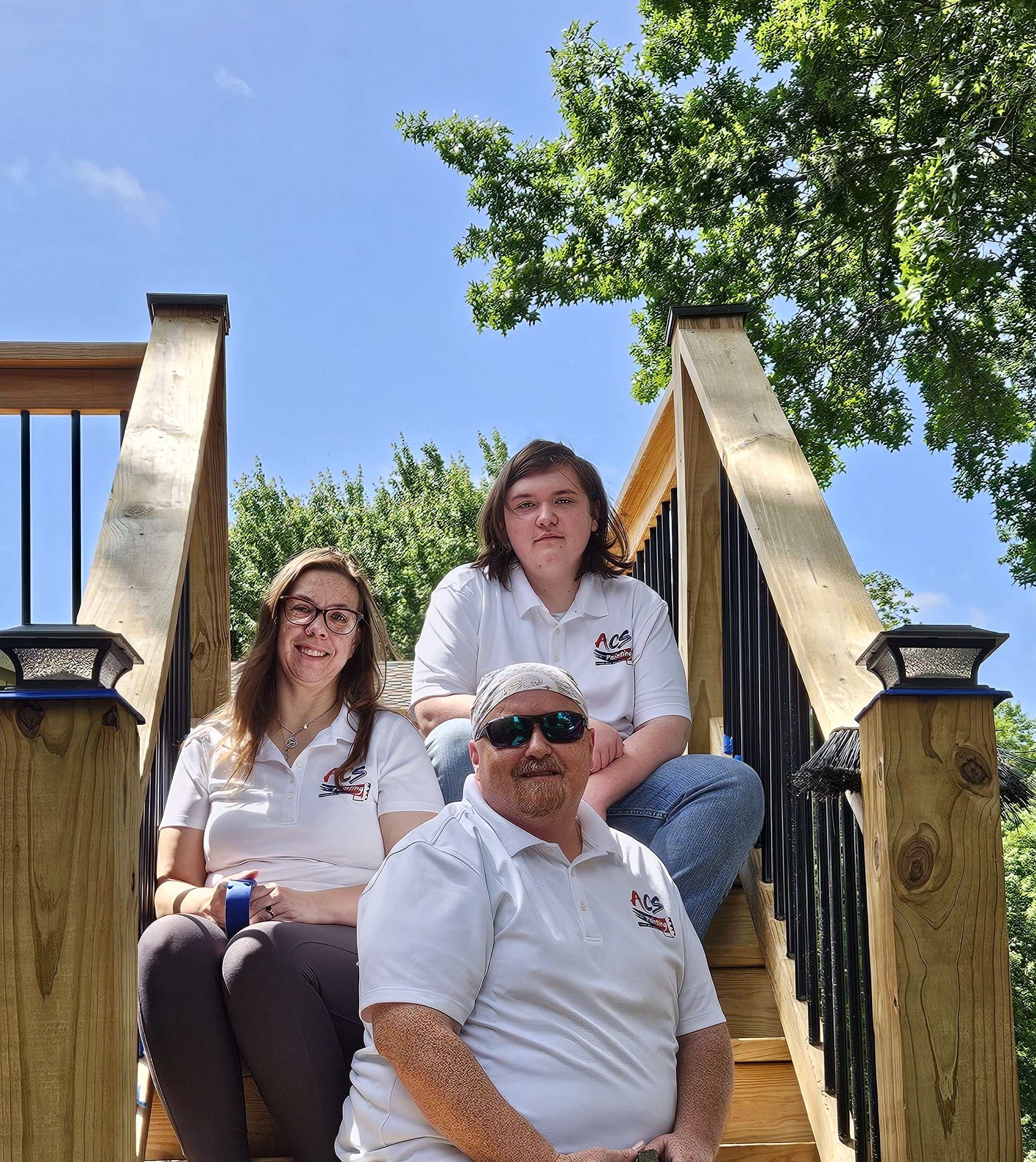 The ACS Painting KC team in white company shirts seated on wooden deck stairs