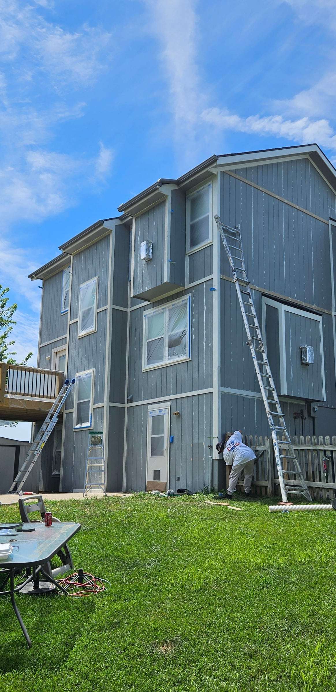 Before: gray-blue panel siding on a three-story rear elevation, ladders in place