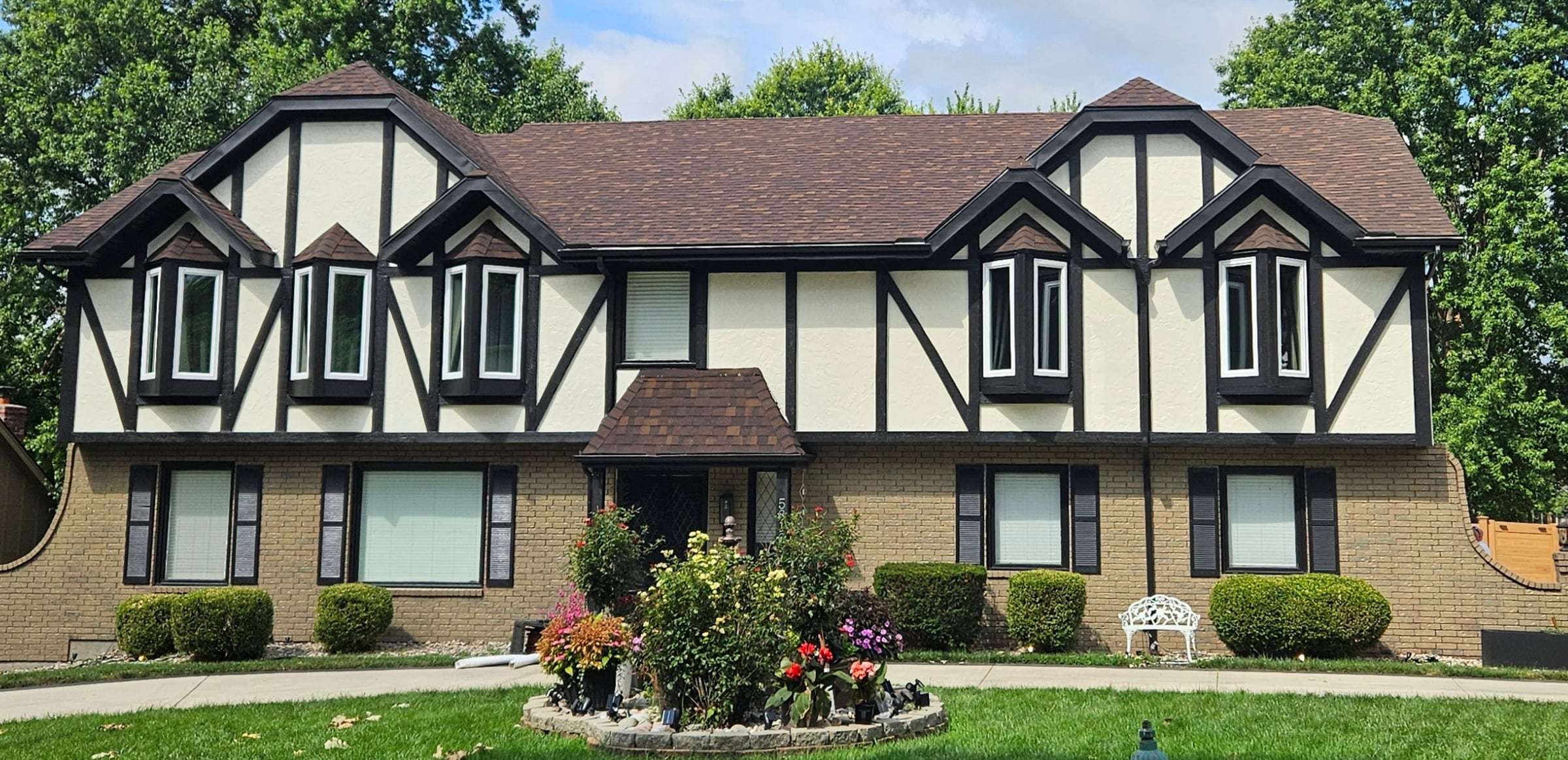 Two-story Tudor-style house after repainting: cream panels, black half-timber trim and buff-toned stained brick